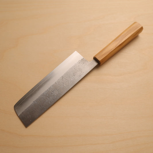A Japanese-style kitchen knife with a textured steel blade and a light brown wooden handle, resting diagonally on a light wood grain surface.
