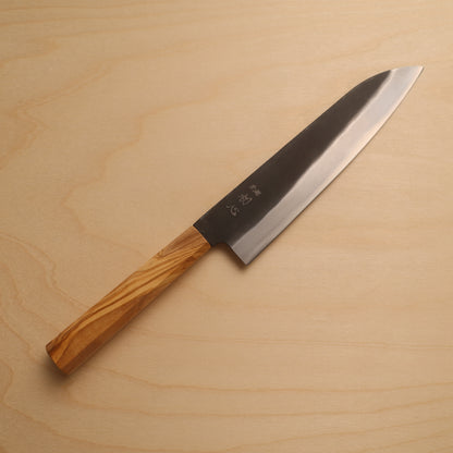 A Japanese-style kitchen knife with a polished steel blade and a natural olive wood handle, placed diagonally on a light wood grain surface.