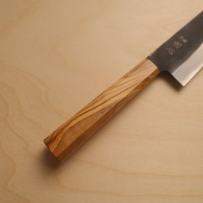 A Japanese kitchen knife with a natural wood handle and a dark steel blade, placed diagonally on a light wood grain surface.