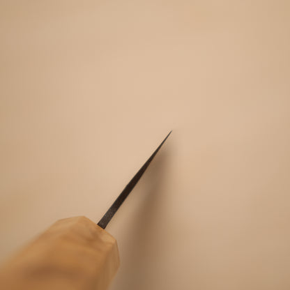 A close-up of a hand holding a long-handled, thin pointed tool, likely a nail file or sharpener, against a plain beige background.