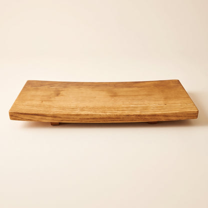 A rectangular wooden serving board with a natural live edge and small feet, shown on a plain beige background.