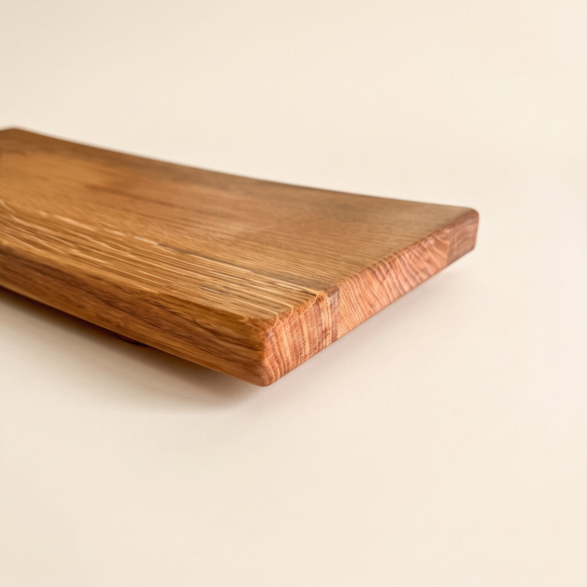 A close-up of a rectangular wooden board with rounded corners, showing a warm medium-brown wood grain and a lighter, slightly pinkish end grain, photographed on a clean off-white background.