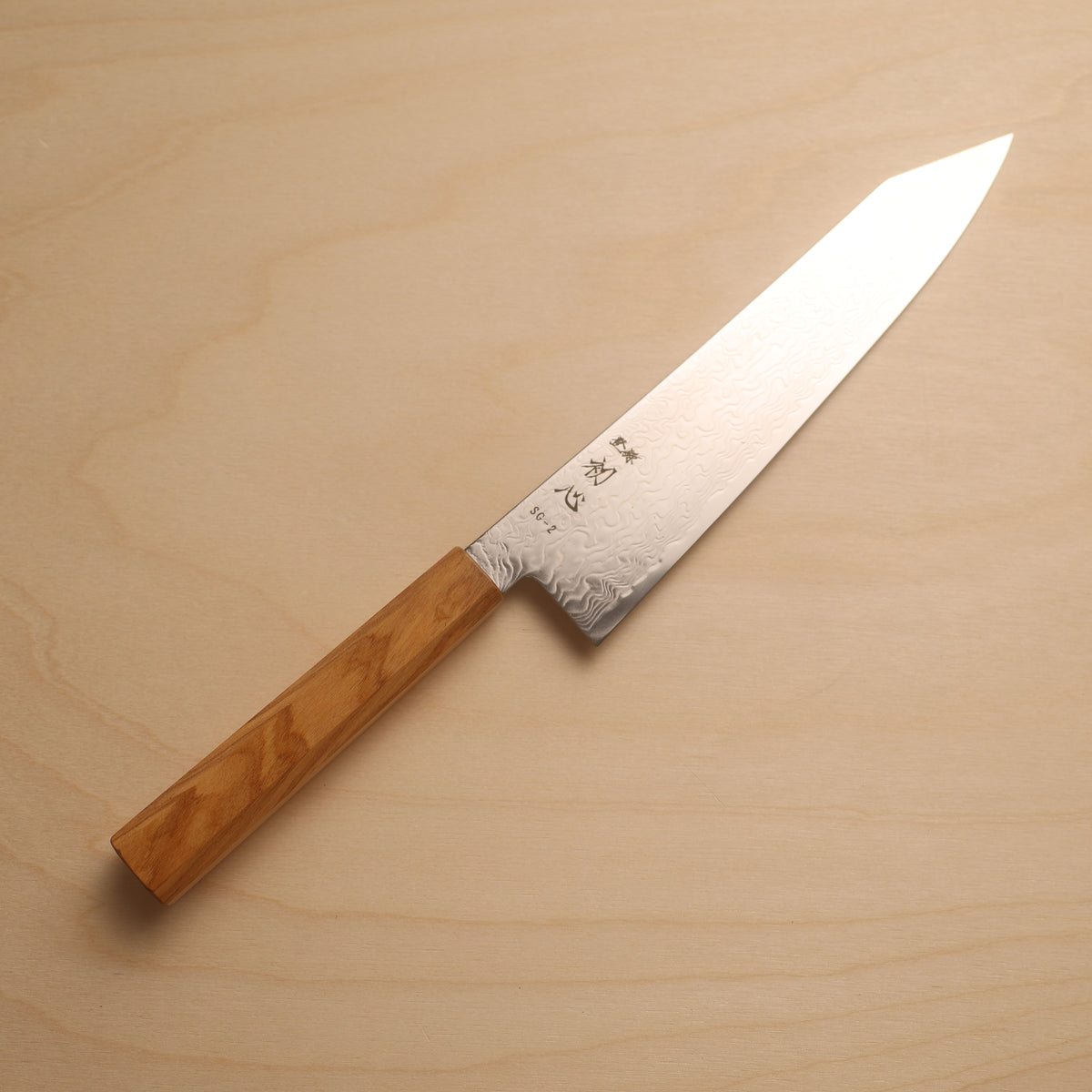 A Japanese kitchen knife with a patterned steel blade and a light brown wooden handle, placed diagonally on a light wood grain background.