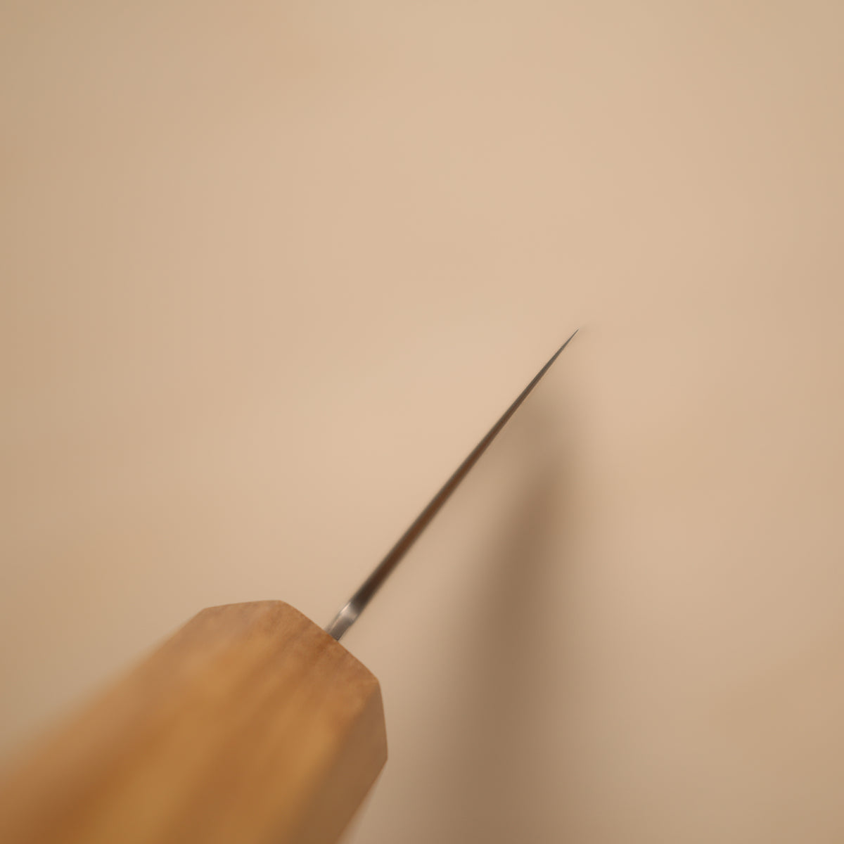 A close-up of a wooden-handled tool with a long, thin metallic prong or needle-like tip, photographed against a plain warm beige background.