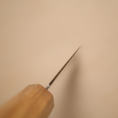 A close-up of a wooden-handled tool with a long, thin metallic prong or needle-like tip, photographed against a plain warm beige background.
