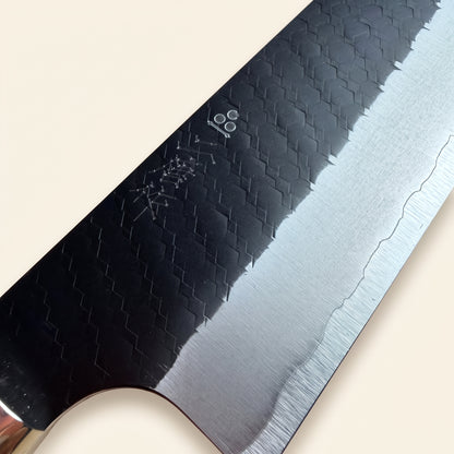 Close-up of hexagonal tsuchime hammer marks and black kurouchi finish on Nigara SG2 Kiritsuke blade with engraved logo