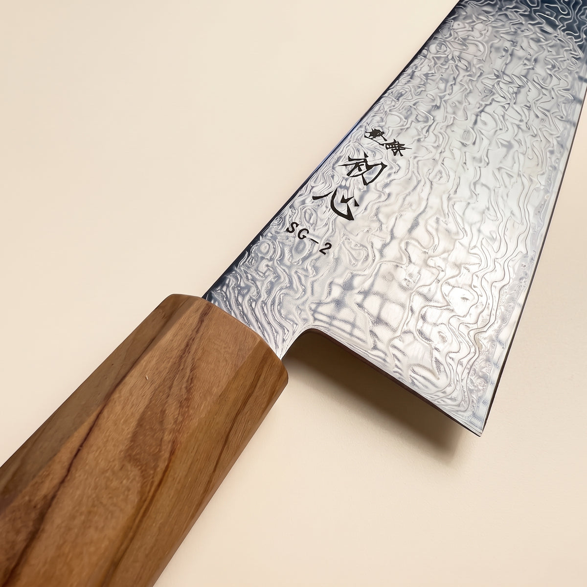 Close-up of Hatsukokoro Ryuhyo high-contrast SG2 damascus pattern and polished migaki blade surface on a dark stone background