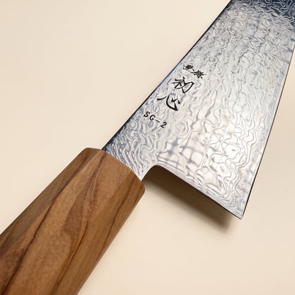 Close-up of Hatsukokoro Ryuhyo high-contrast SG2 damascus pattern and polished migaki blade surface on a dark stone background